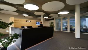 Eingangsbereich der FSM AG mit einem modernen Empfangstresen, einer hölzernen Wand mit Firmenlogo und großen Glasfenstern im Hintergrund.