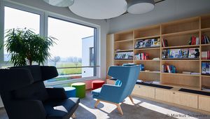Modern eingerichteter Aufenthaltsbereich im Firmengebäude der FSM AG mit Sesseln, einem Regal voller Bücher und Zeitschriften sowie großen Fenstern mit Blick auf die Landschaft.